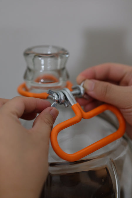 Orange FastRack carboy neck handle carrier with ergonomic grip and secure straps for easy transport of glass carboys.